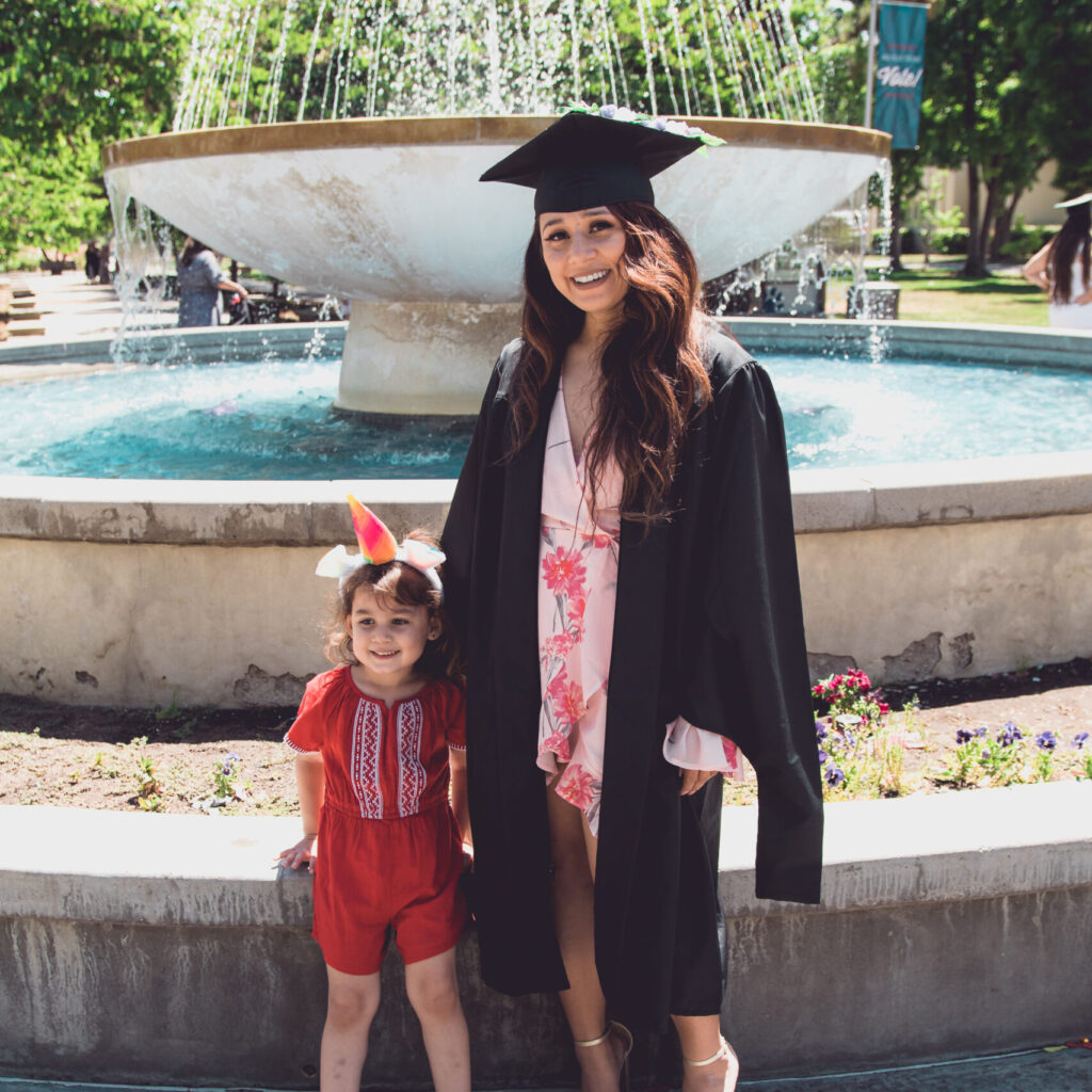 A woman in a graduation cap and gown standing with a child.